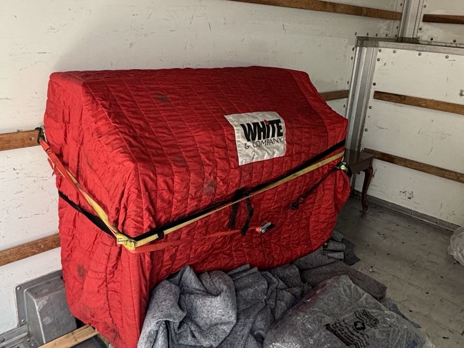 A piano wrapped in moving pads and strapped in place inside a moving truck